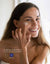 Retrato de una joven sonriente aplicándose crema ium en la mejilla sobre un fondo de baño
